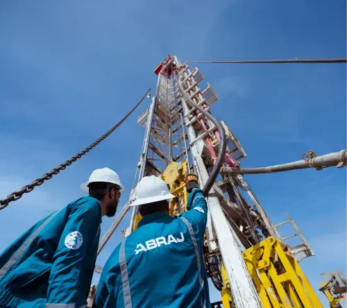 ABRAJ crew members looking up at a drilling mast against a clear Omani sky